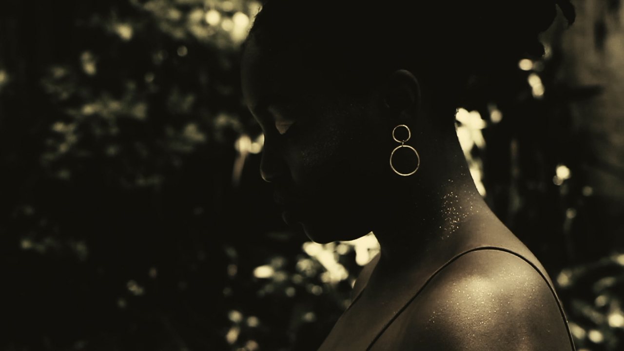 Profile of the face of Beatriz, lit from behind, gold hoop earrings