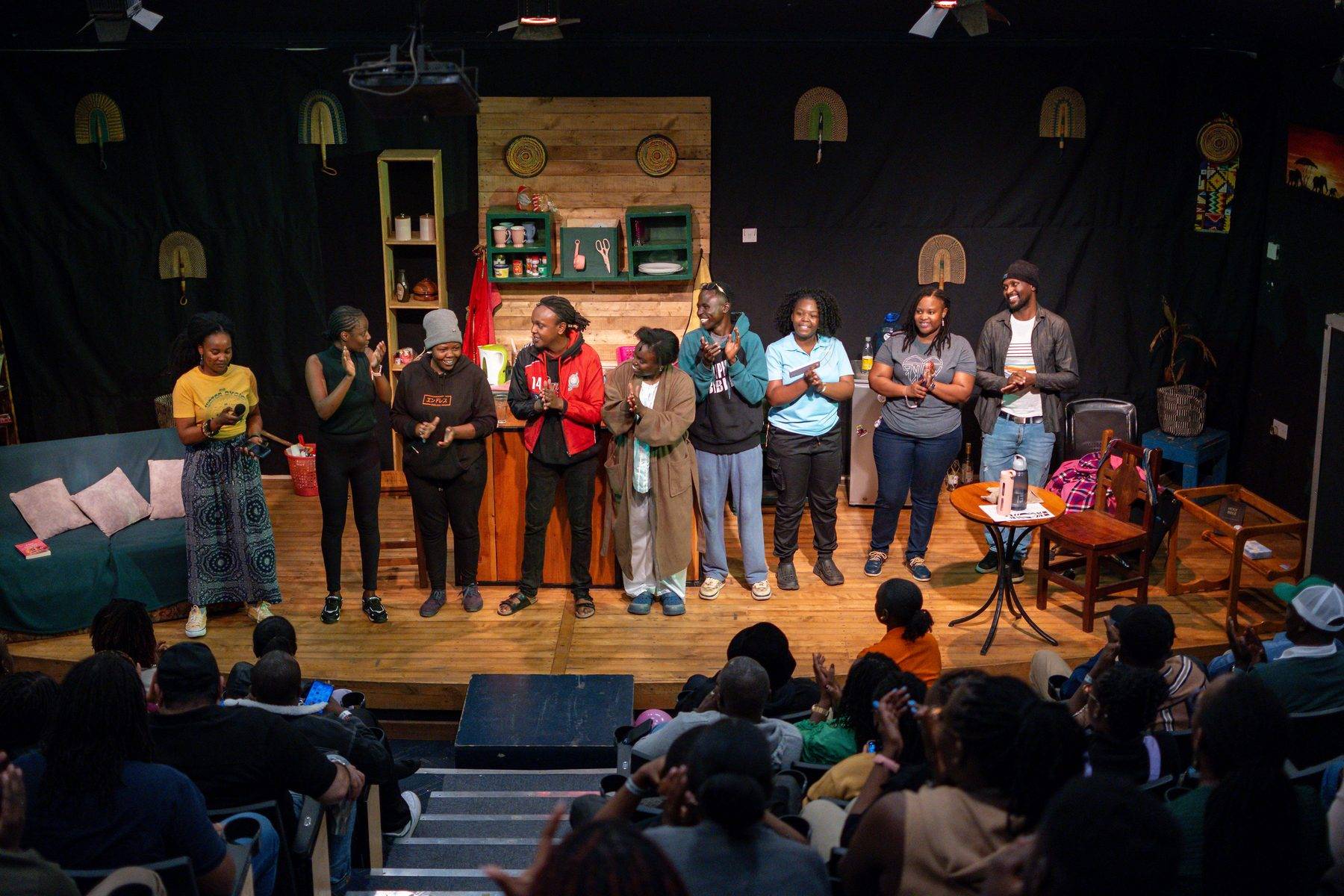 The company stands in a line across the stage applauding at the curtain call