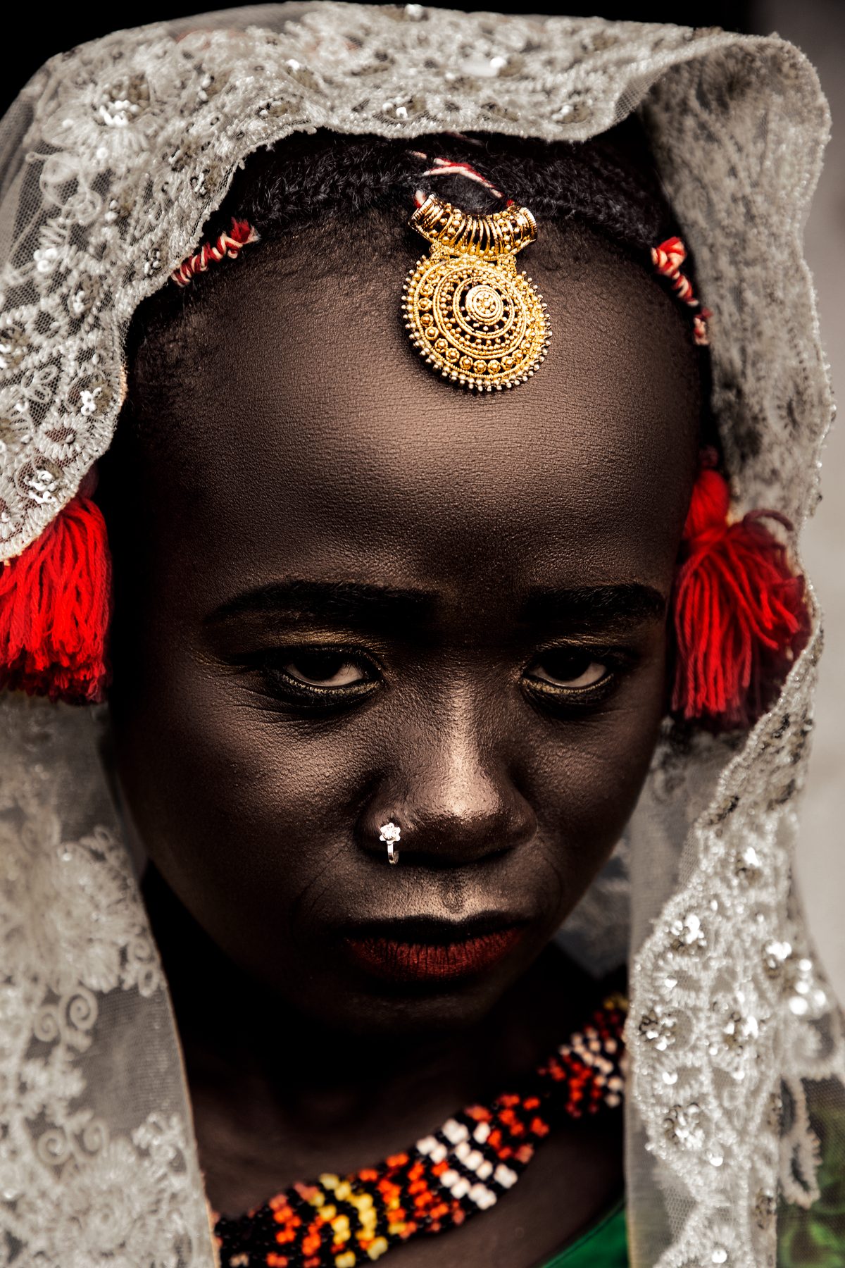 Portrait of a young woman in a white lace veil, with a gold ornament on her forehead and a beaded collar