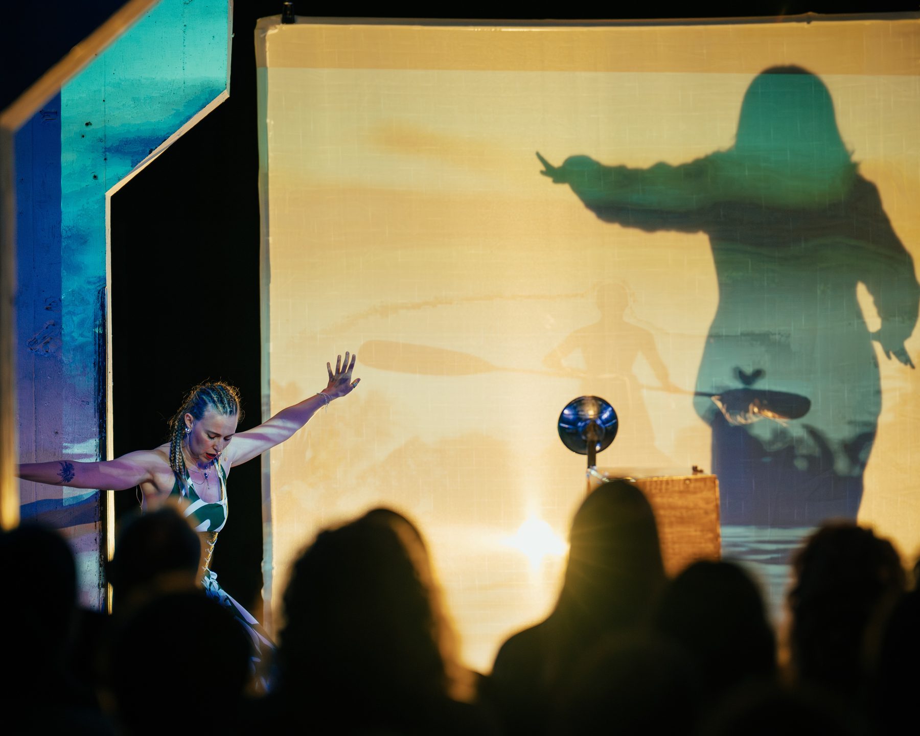 A performer dances in front of a backlit screen, her shadow thrown large across it, beside the Camera Absurda on its stand